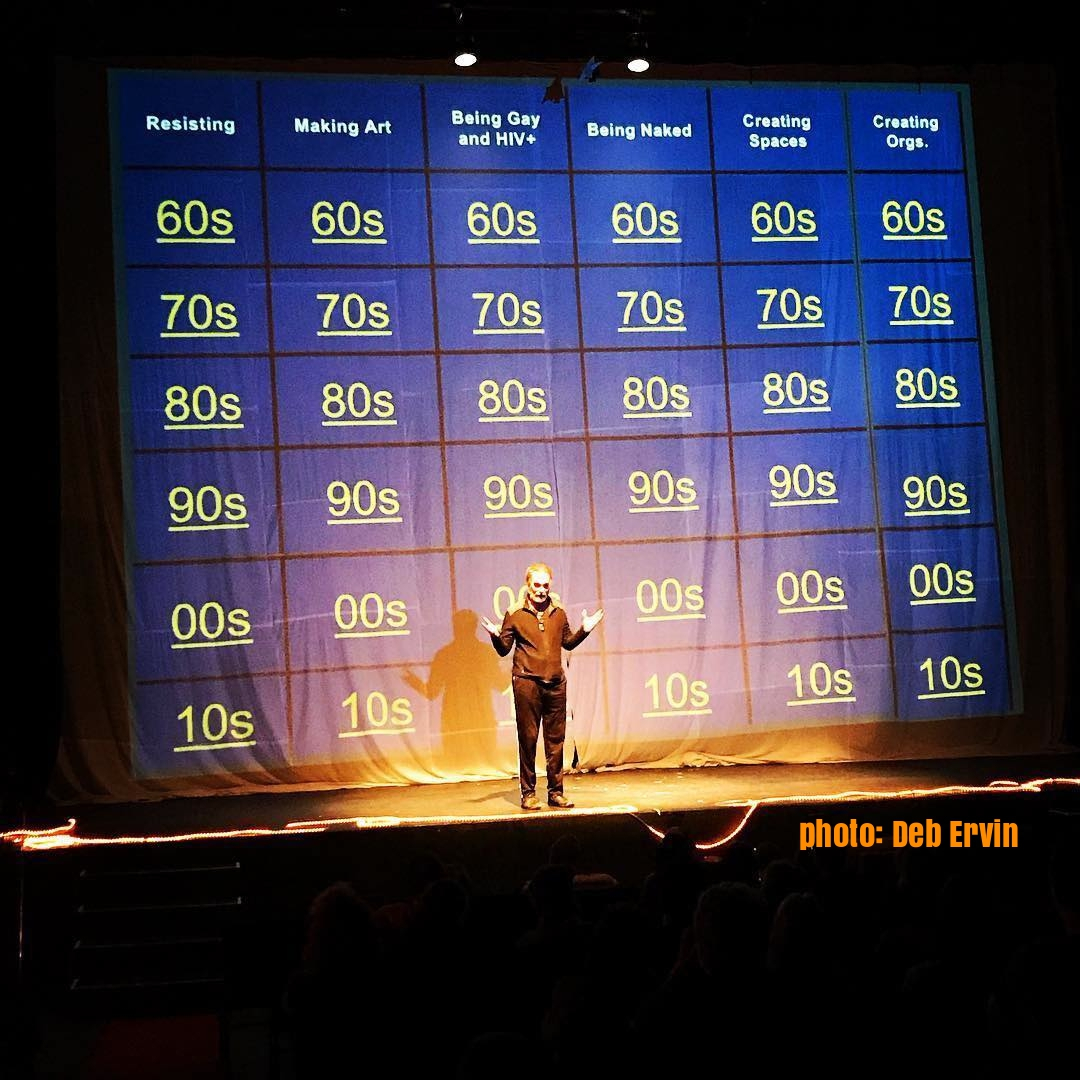 Performer Patrick Scully standing on stage in front of a Jeopardy board.
